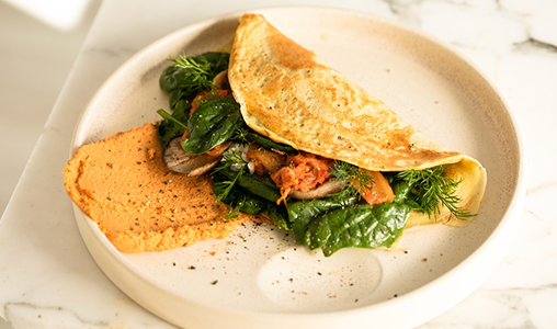 A savory omelette folded over fresh greens, served with a side of spiced hummus on a beige ceramic plate.